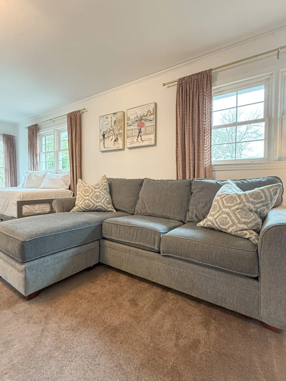 A spacious living area featuring a gray sectional sofa adorned with decorative pillows. The artwork on the wall and soft curtains over the window create a cozy yet professional atmosphere, ideal for relaxing or working in comfort.