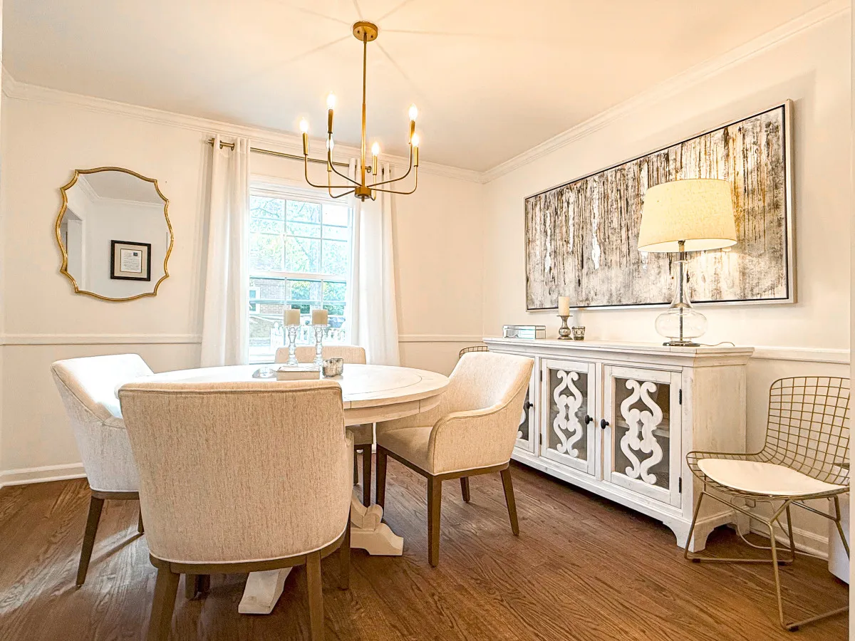 A stylish dining area with a round table surrounded by white chairs, a striking chandelier overhead, tasteful wall art, and a decorative cabinet. The space is welcoming, perfect for shared meals, morning coffee, or memorable celebrations with loved ones.