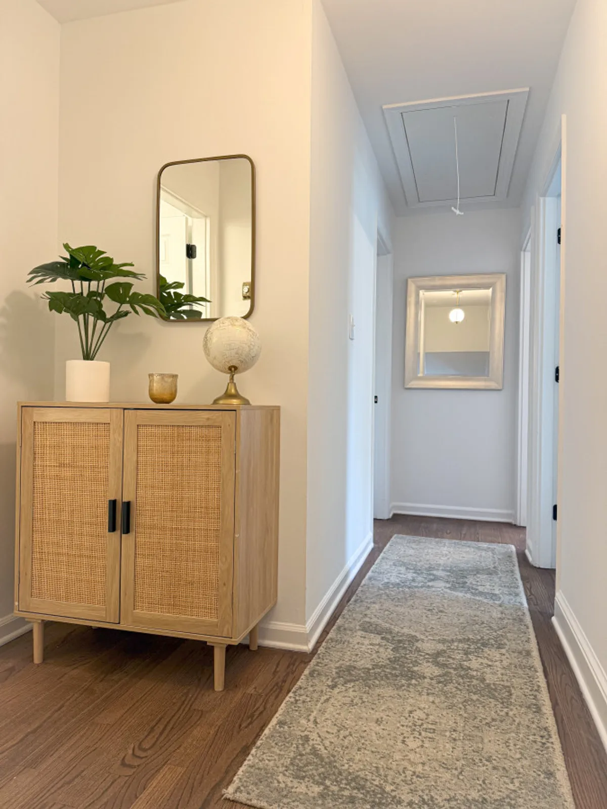 A calm and welcoming general circulation area with a wooden cabinet, large mirror, decorative globe, and a potted plant. The space exudes tidiness and an organized, professionally managed feel, perfect for welcoming guests or starting your stay.