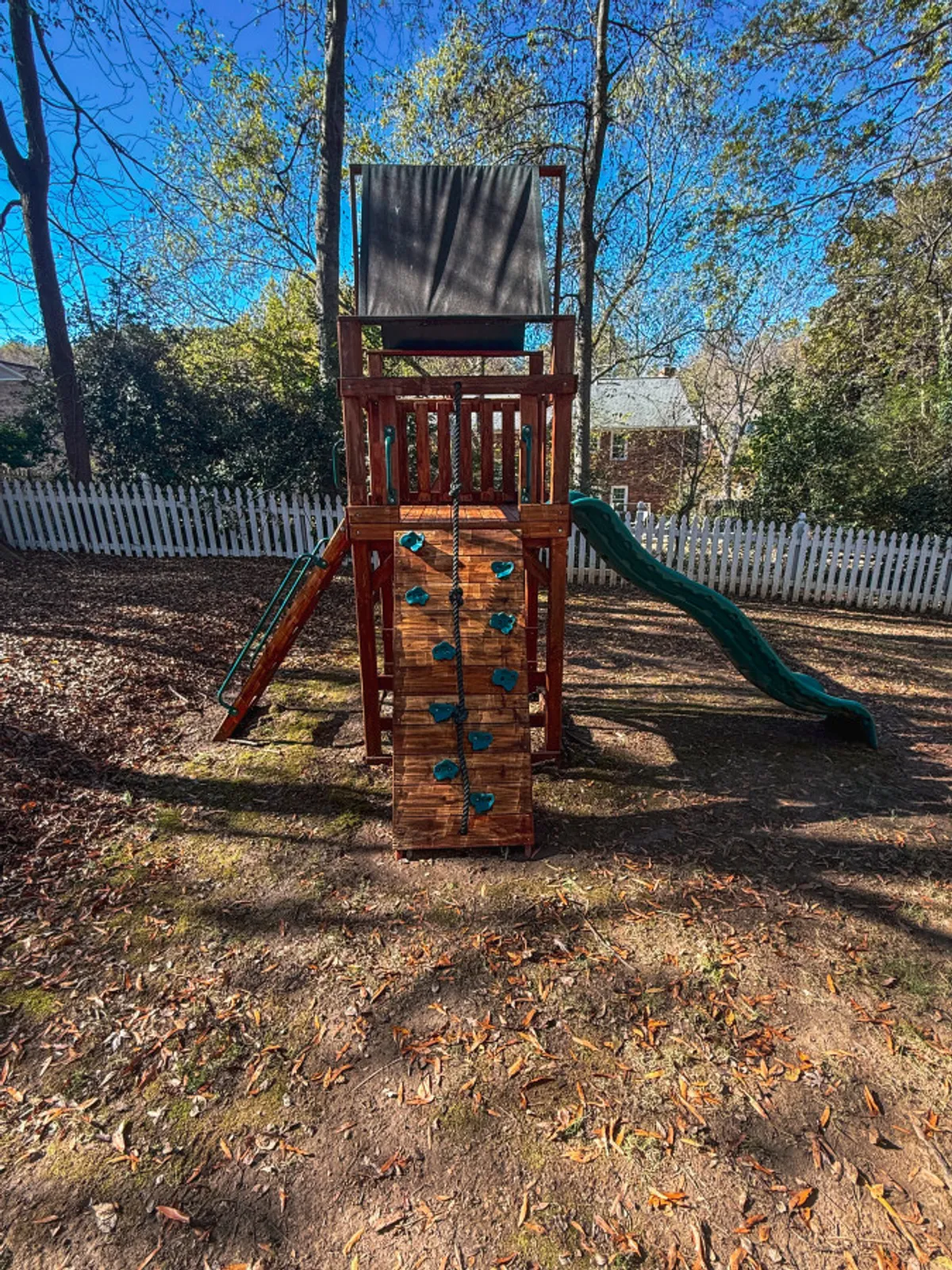 A vibrant backyard scene featuring a playground structure with a slide and climbing wall, inviting children to play and explore. The fenced-in yard and spacious area offer a safe and joyful environment for families, perfect for outdoor adventures and imaginative play.