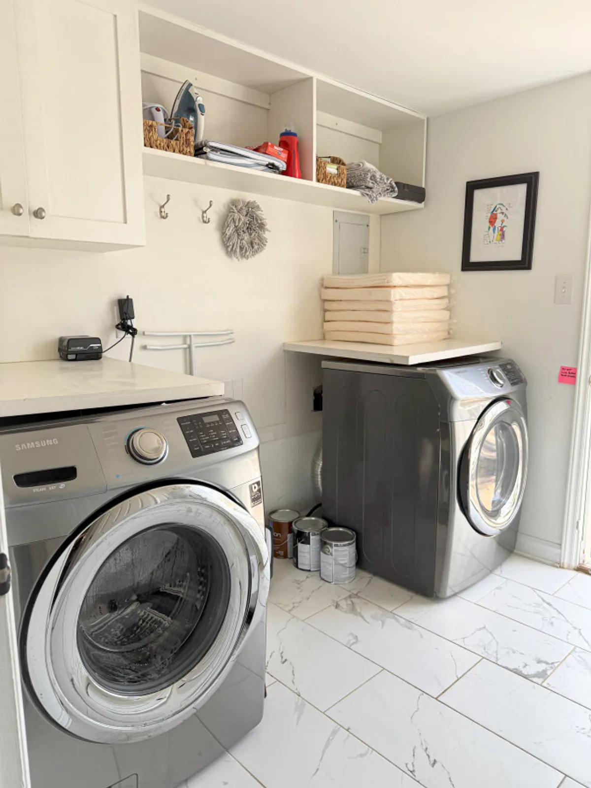 A tidy laundry space with a modern washing machine and dryer, thoughtfully organized shelves, and decorative artwork on the wall, conveying efficiency and the convenience of in-unit laundry.