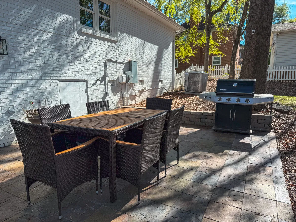 This image features an inviting outdoor dining table set amidst lush greenery, with a prominent Charbroil grill positioned nearby. The scene is bathed in sunlight, suggesting a perfect environment for family barbecues, outdoor dining, and relaxed gatherings in a private, fenced backyard setting.