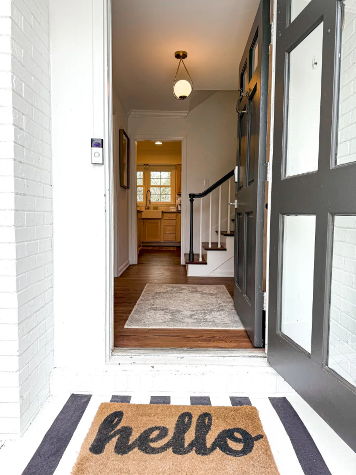 A view of the front door and entryway, featuring a welcoming mat, a well-lit staircase, and a glimpse into the kitchen beyond. The area is bright, tidy, and immediately inviting, with decor that sets a professional and warm tone upon arrival.